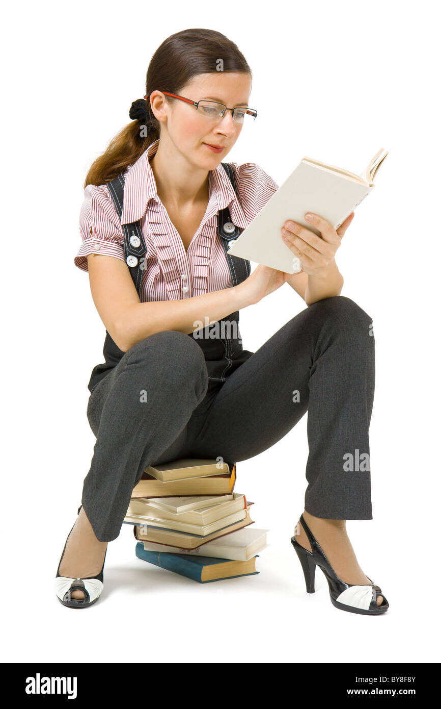 young girl with glasses sitting on a pile of books and reading Stock ...