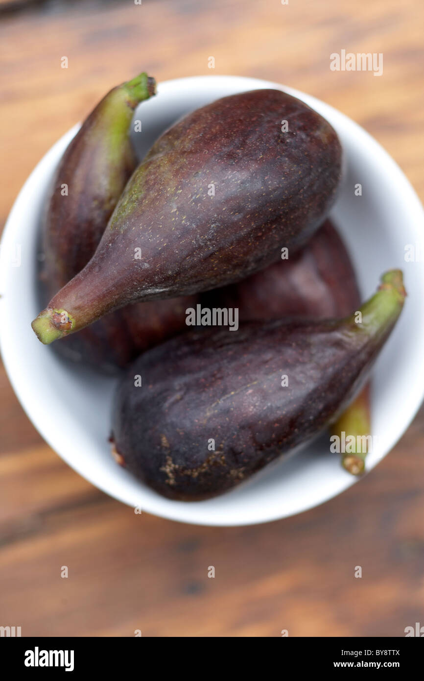 Figs in a small white bowl on wooden table Stock Photo