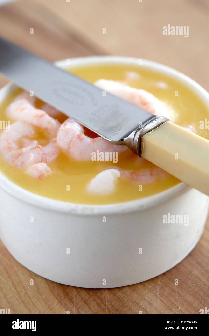 Potted prawns in white container on wooden background with knife Stock Photo