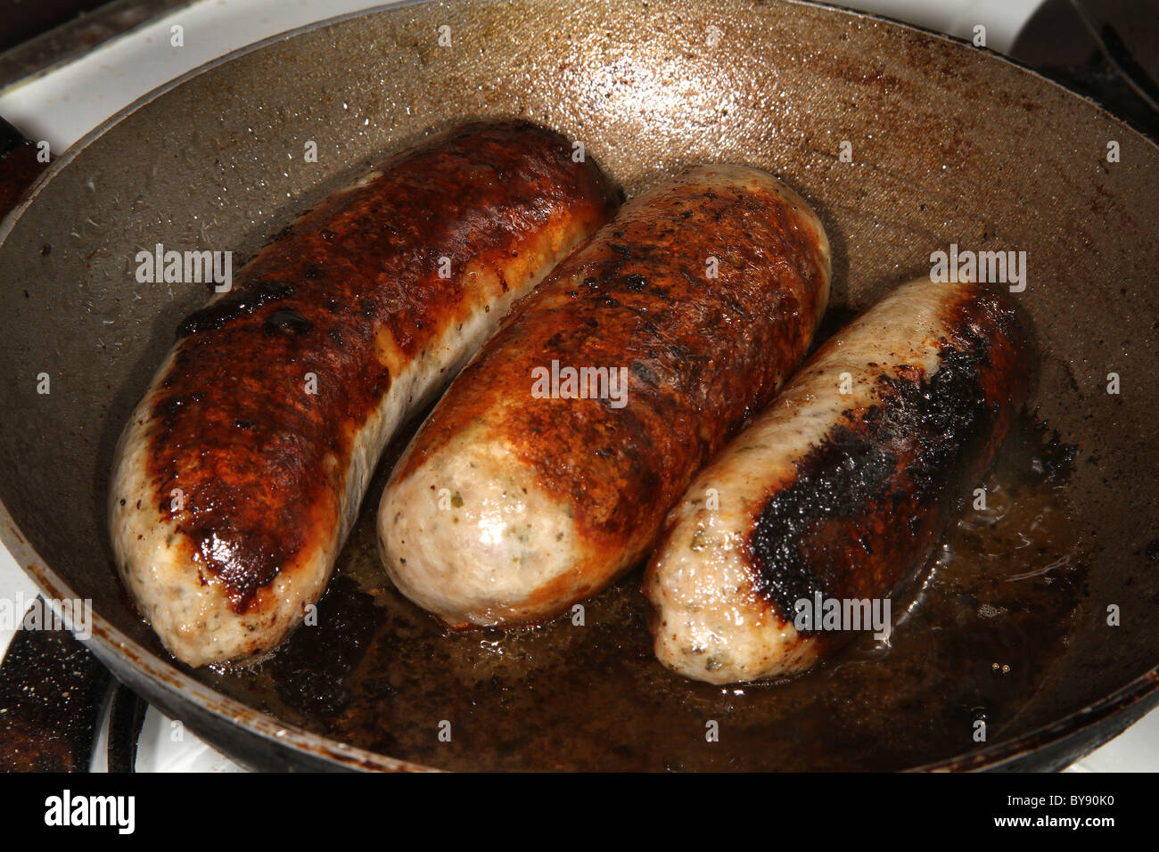 Three large Lincolnshire Pork sausages cooking in frying pan Stock