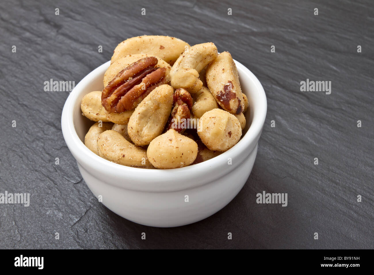 Mixed Salted Nuts in bowl on dark grey slate background. Stock Photo