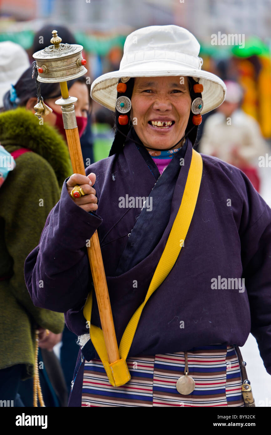 Tibetan woman pilgrim in white hat spinning large prayer wheel in the