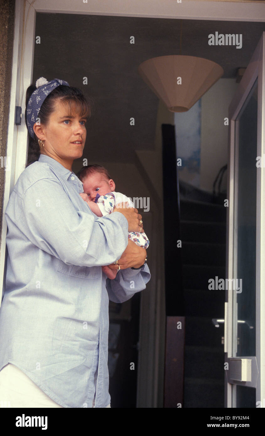 unhappy mother standing at open door holding her baby Stock Photo