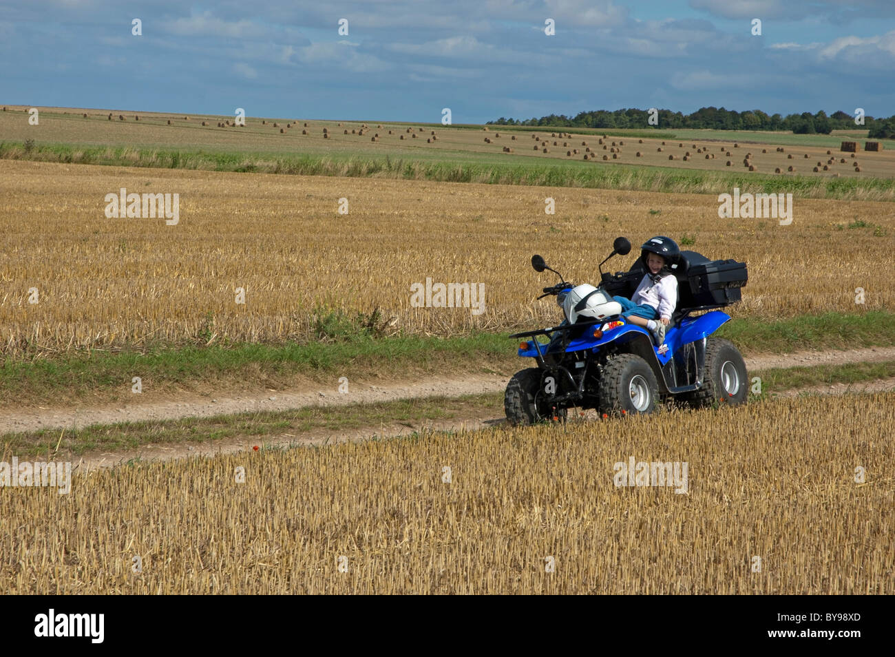 Four year old girl sitting on a quadbike parked in the middle of a harvested wheat field, Normandy, France. Stock Photo