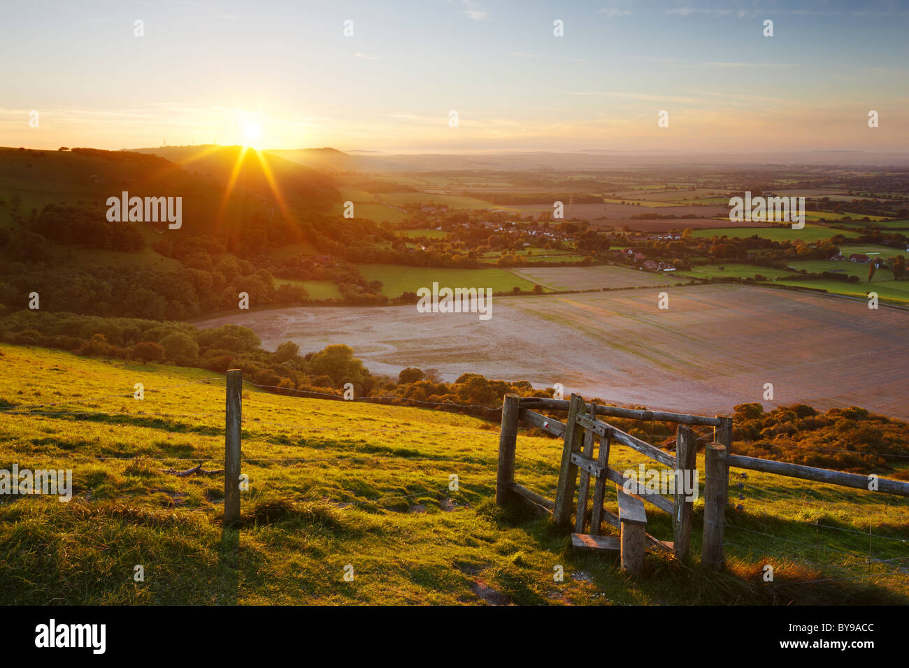 Stile with views across the West Sussex countryside. The evening sun making its descent behind the undulating Hillside. Stock Photo