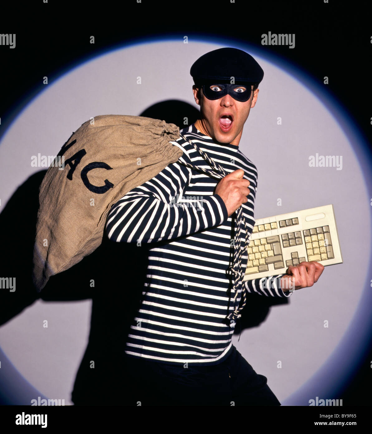 Burglar in traditional costume. Burglar with swag bag and keyboard stealing a computer Stock Photo