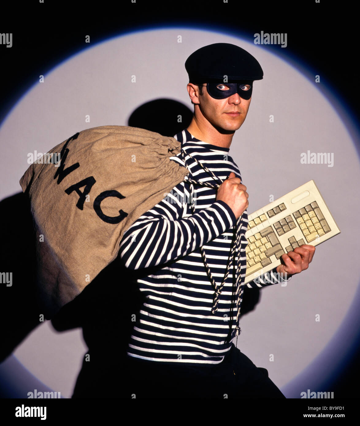 Burglar in traditional costume with swag bag and keyboard stealing a computer Stock Photo