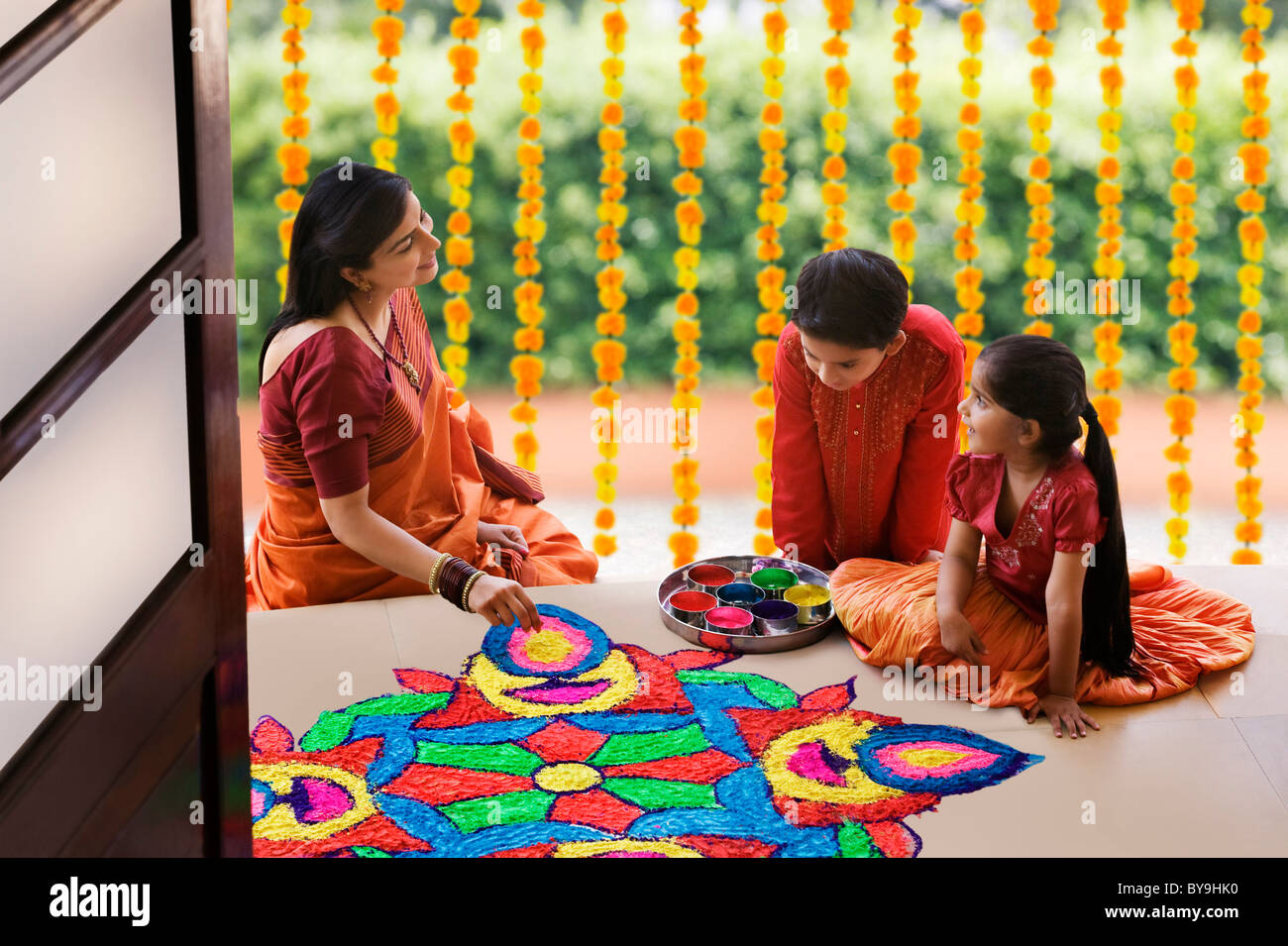 Woman making a rangoli while her children watch Stock Photo