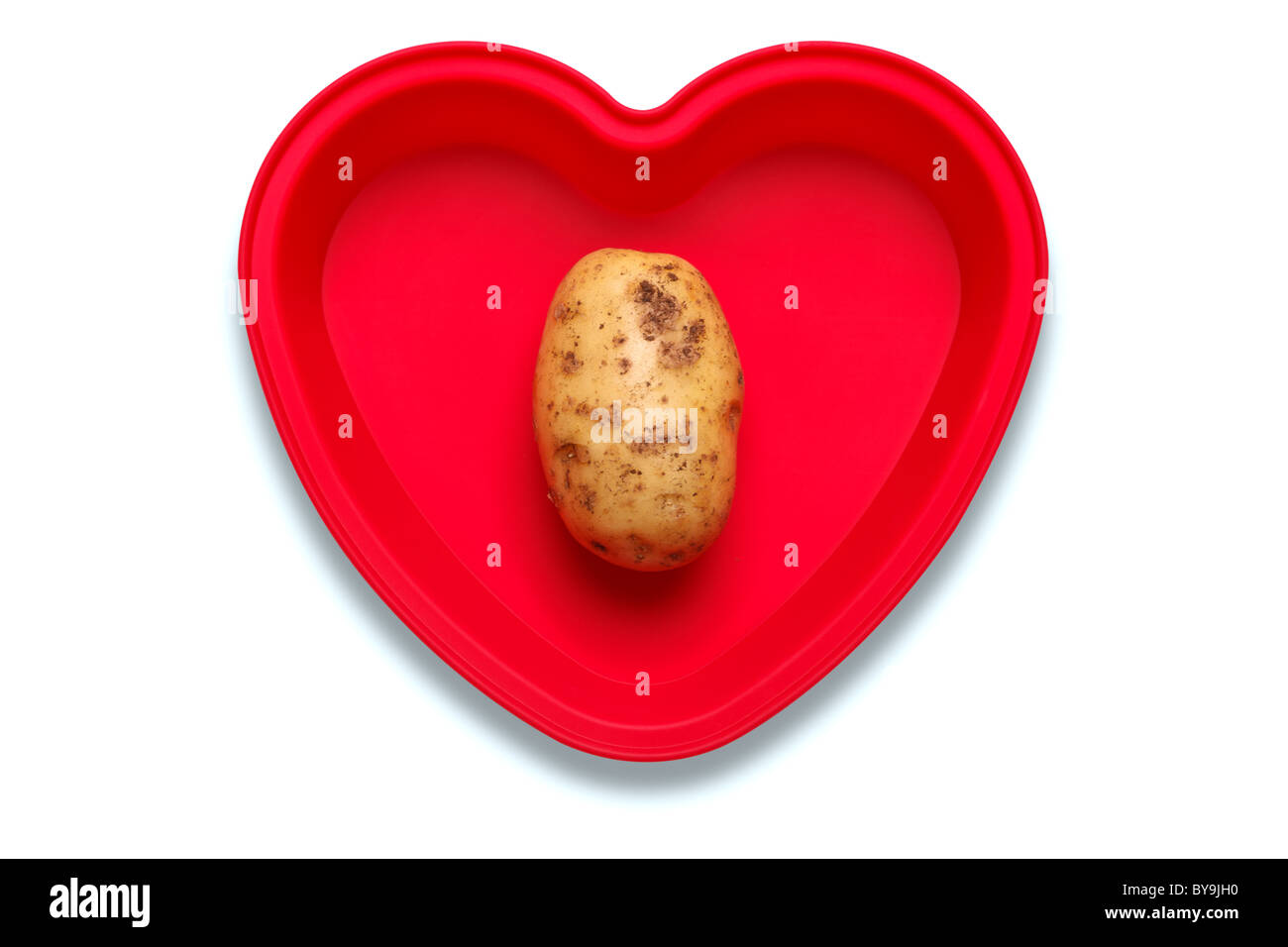 Conceptual photo of a potato in a heart shaped dish to represent a love of the vegetable, isolated on a white background Stock Photo