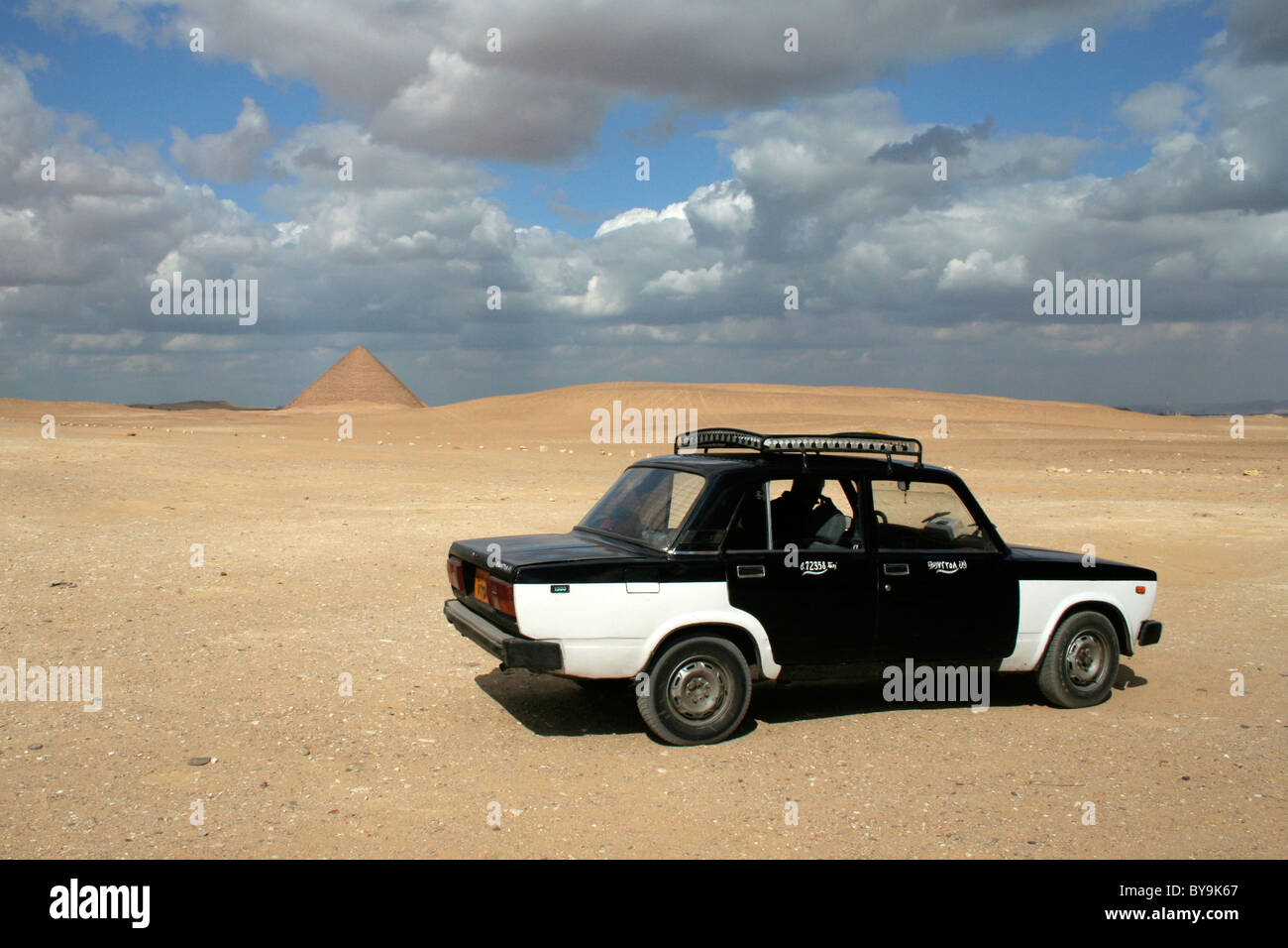 A black and white Egyptian taxi waiting in the desert with the Red Pyramid in the background near Cairo Stock Photo