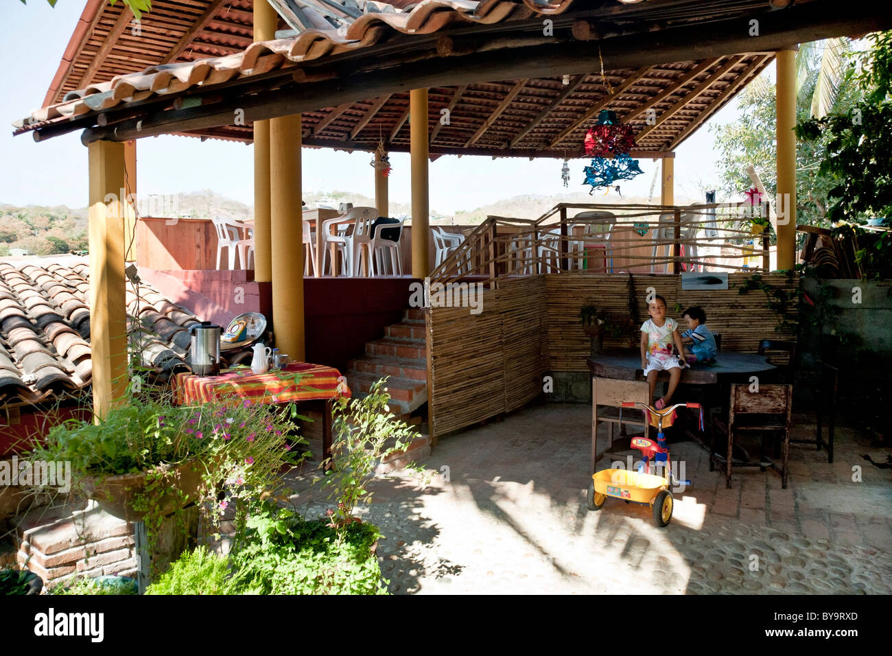 small Mexican girl & baby brother play on table in airy roofed outside dining pavilion of hillside guest house Puerto Angel Stock Photo