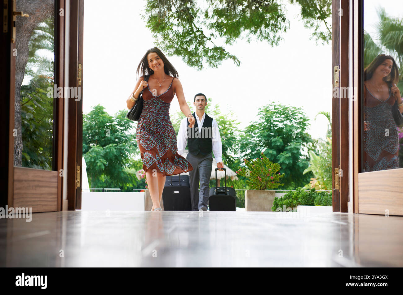 Woman entering hotel man carrying bags Stock Photo