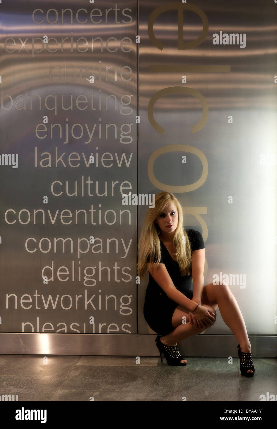 Young woman with long blonde hair, posing in front of a wall with words Stock Photo