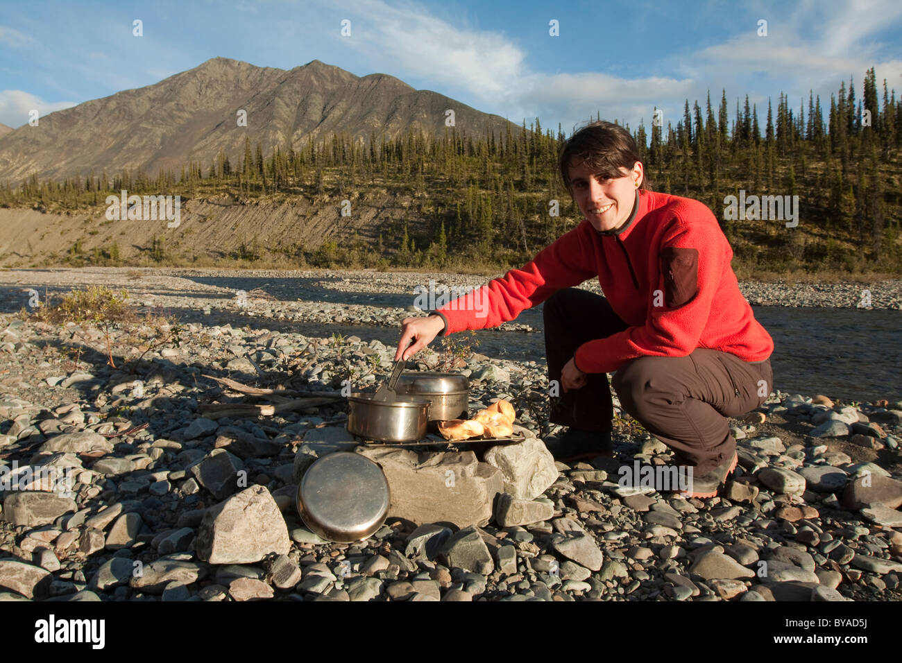 Young woman cooking on a camp fire, camping, gravel bar, Northern Mackenzie Mountains and Wind