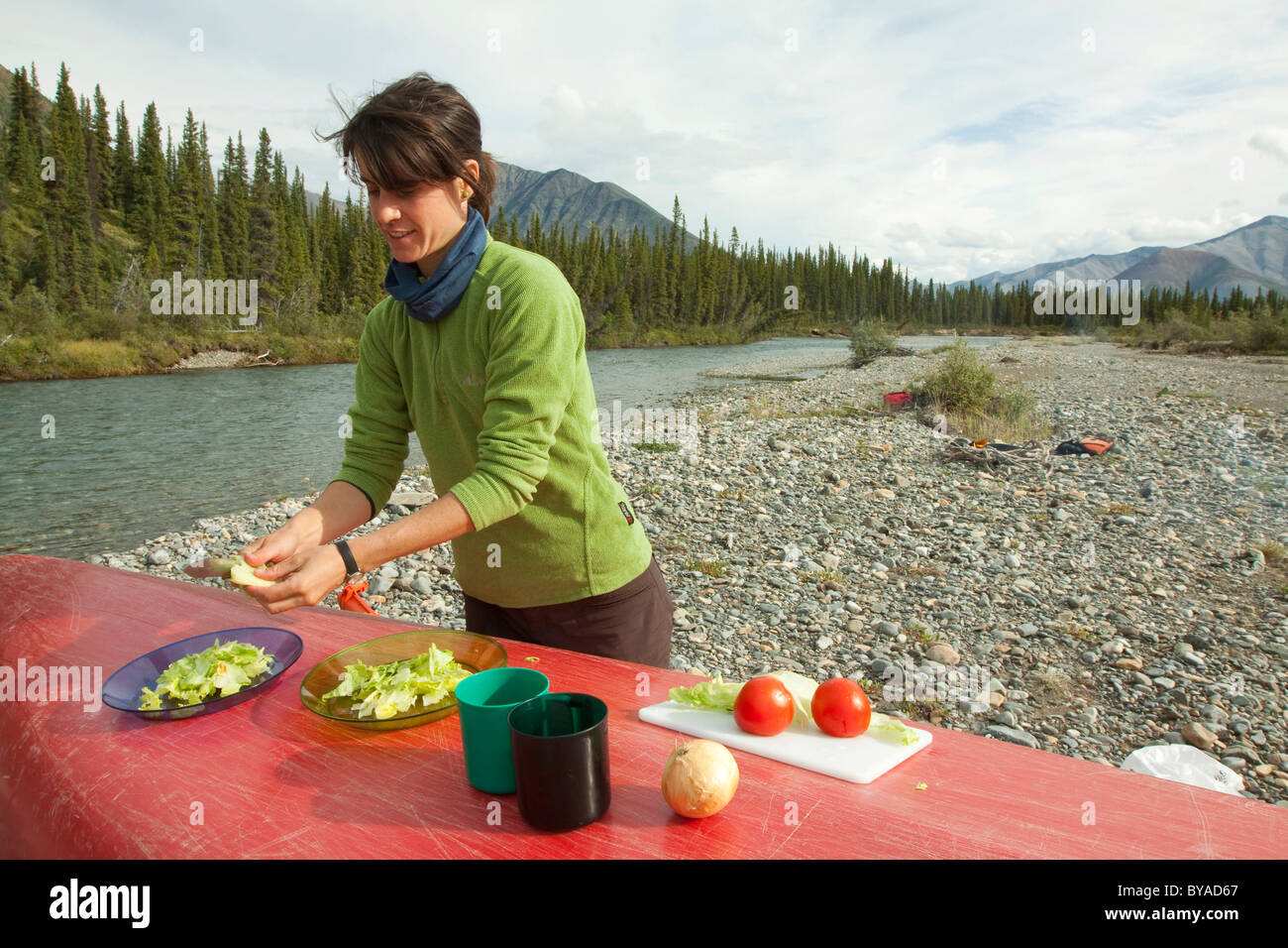 Young woman cooking, cutting vegetables, preparing a salad, using an upside down canoe as table