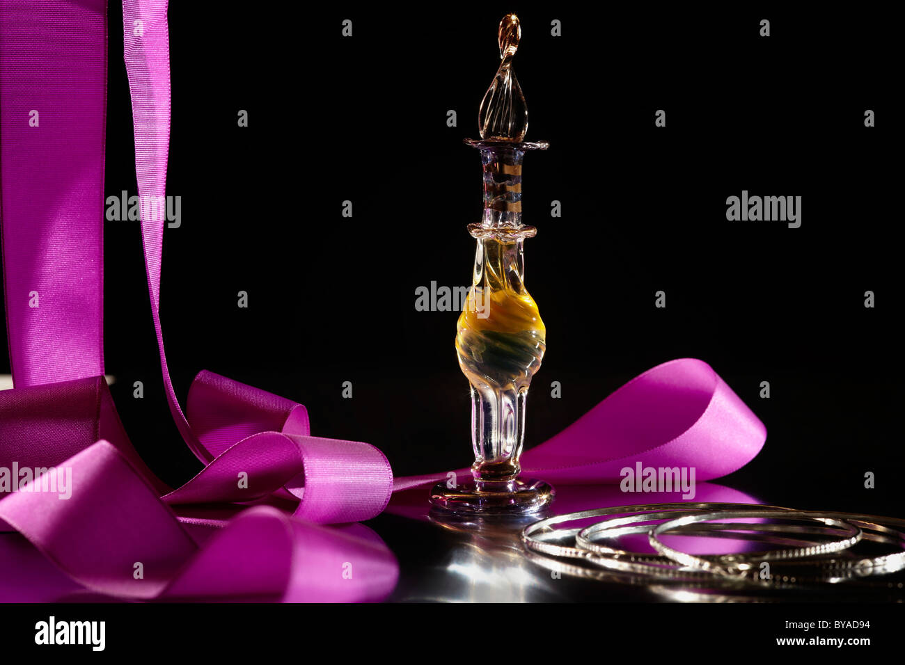 Perfume bottle on a mirrored surface, with bracelets and a pink ribbon Stock Photo