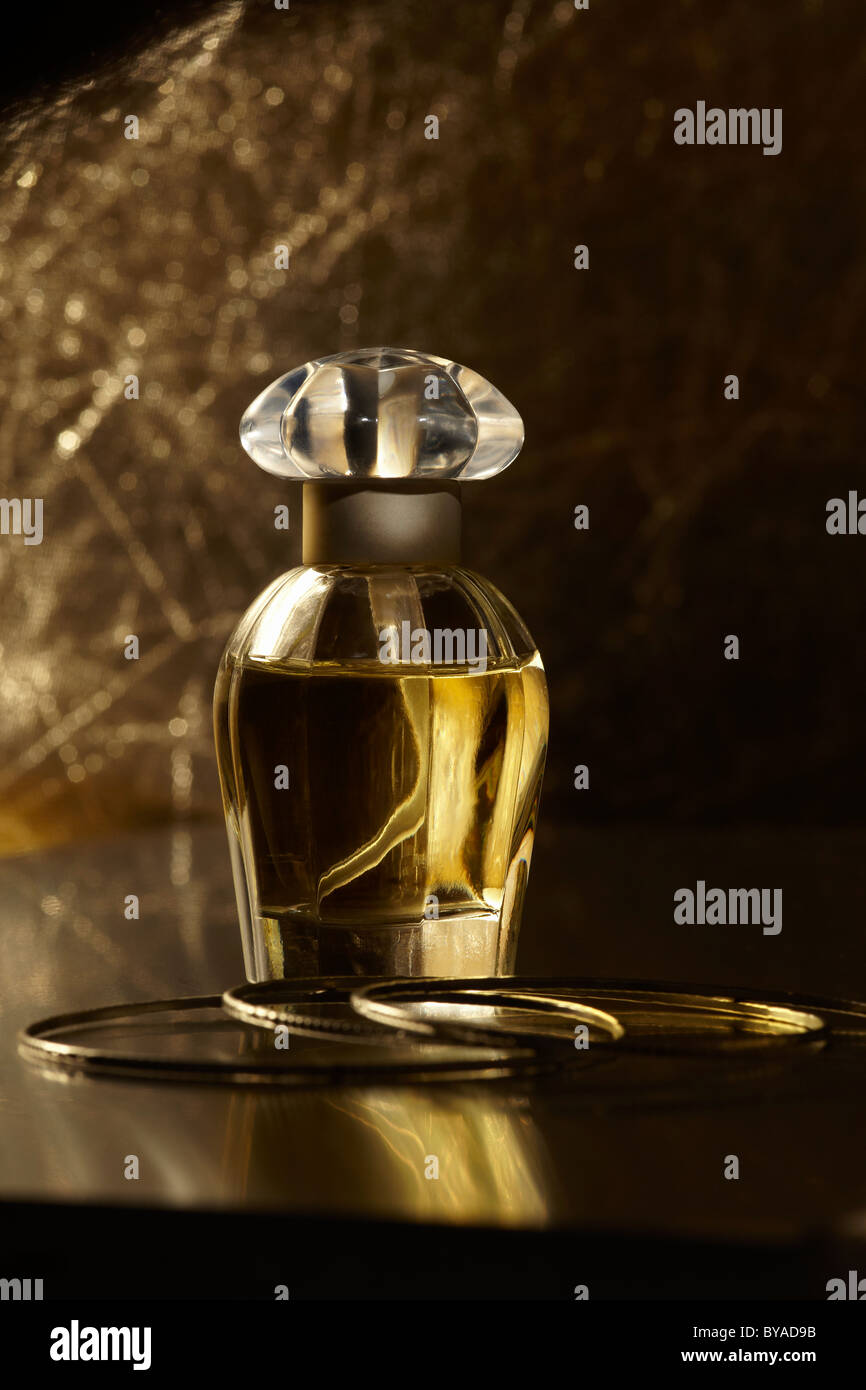 Perfume bottle on a mirrored surface, with gold bracelets Stock Photo