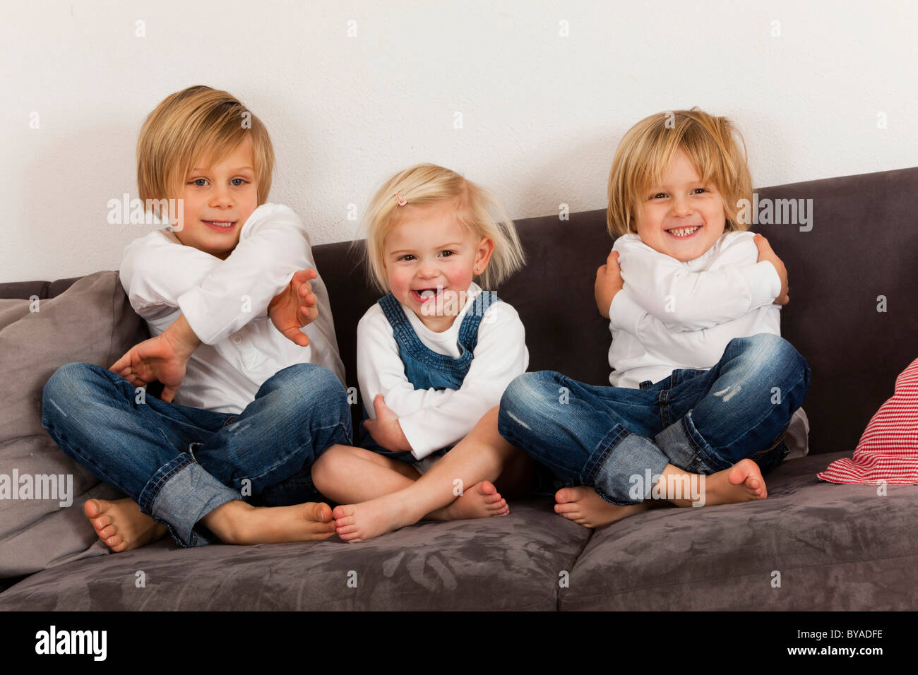 2 boys, 7 and 4 years, and a girl, 1.5 years sitting cross-legged Stock Photo