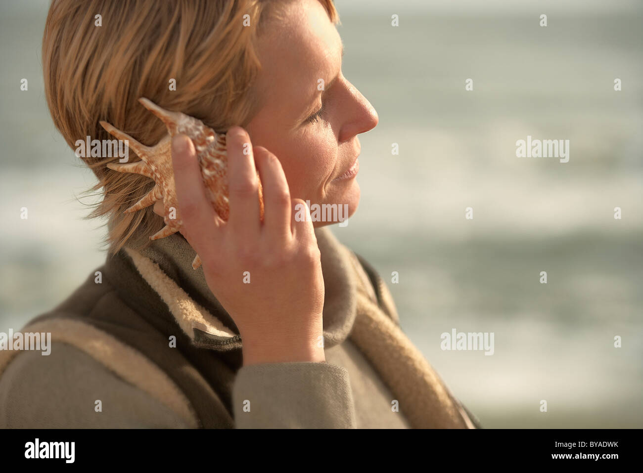 Woman by sea, listening in seashell Stock Photo