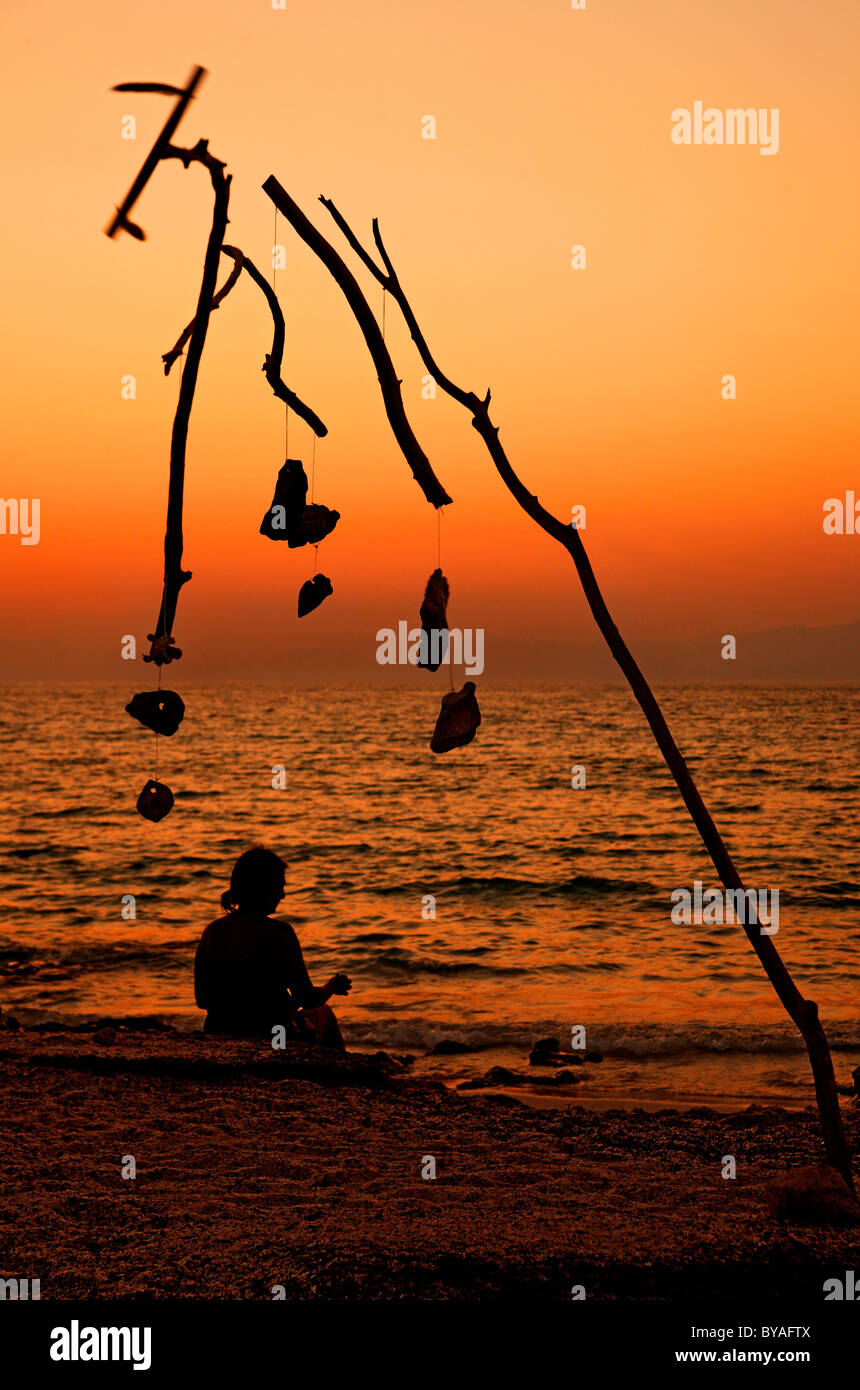 A lonely lady is enjoying the sunset close to a strange 'sculpture' that looks like Calder's mobiles. Chrissi island, Crete Stock Photo