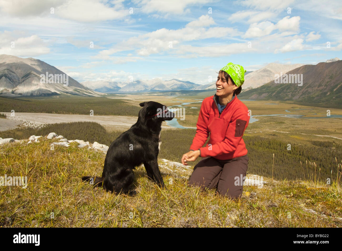 Young woman playing with her dog, Alaskan Husky, sled dog, panorama, Wind River valley and Mackenzie Mountains behind Stock Photo