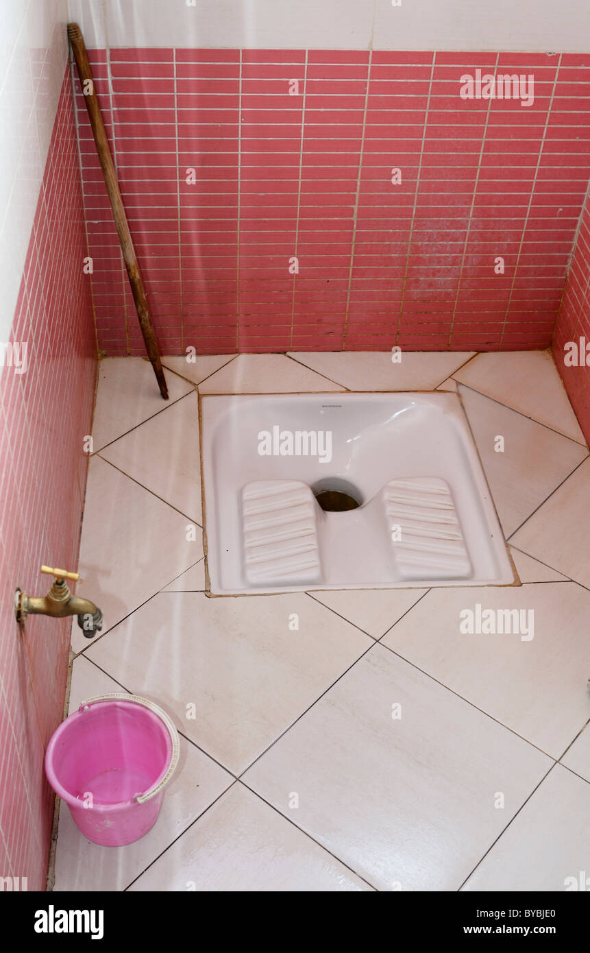 Pink tiled mens restroom with squat toilet fixture with water bucket and stick in Morocco Stock Photo