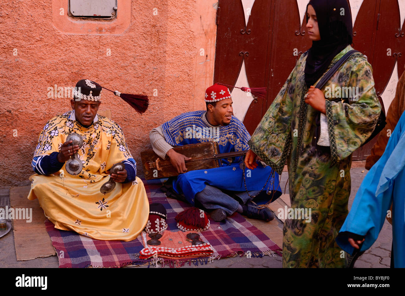 Happy Gnawa street musicians in Marrakesh swinging their tarboosh tassels in time with the music and women passersby Morocco Stock Photo