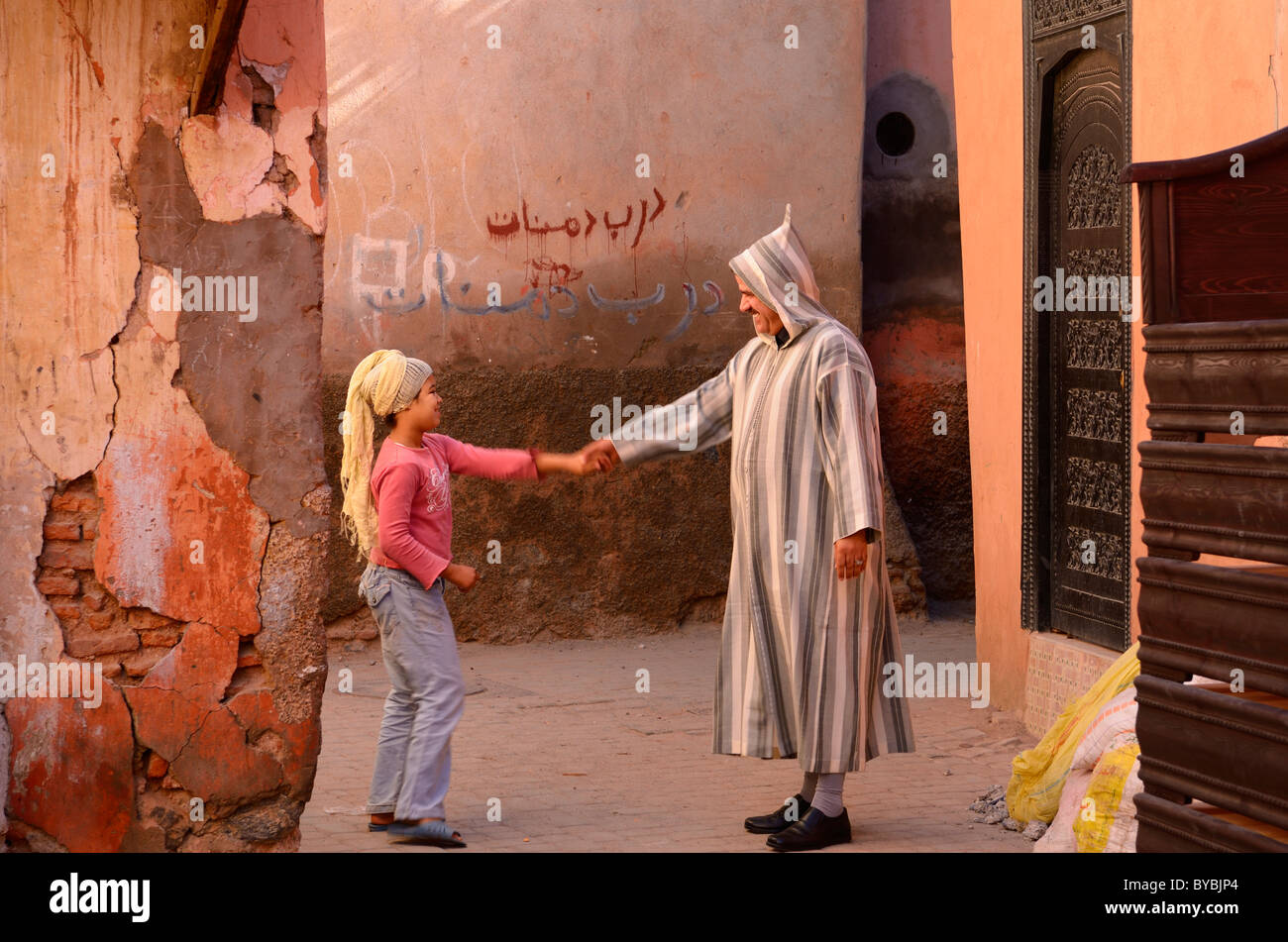 Moroccan man in djellaba greeting a young girl with headscarf in souk of Marrakech Stock Photo