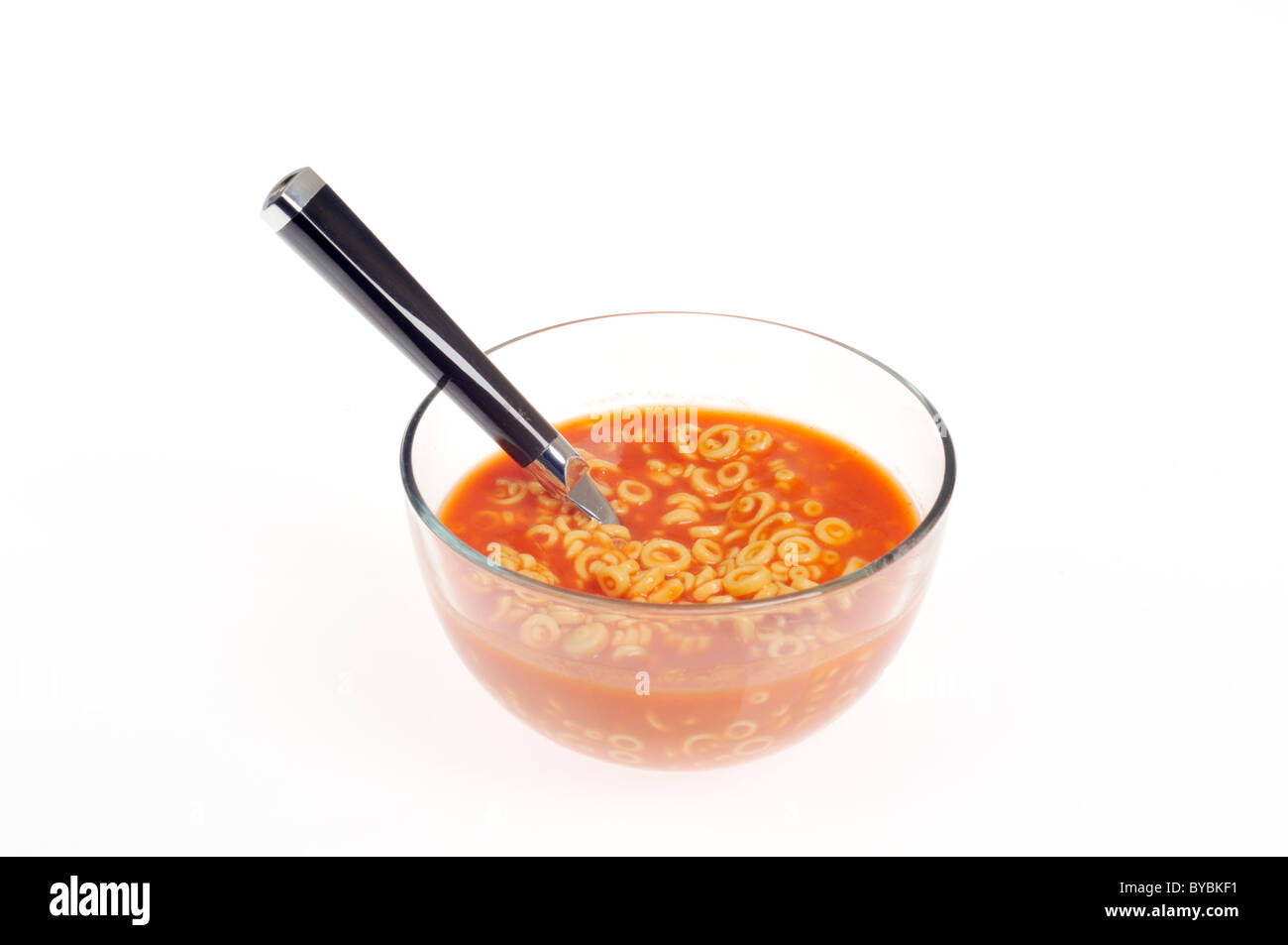 Clear glass bowl of Spaghetti-O's hoops and tomato sauce with spoon on white background cutout Stock Photo