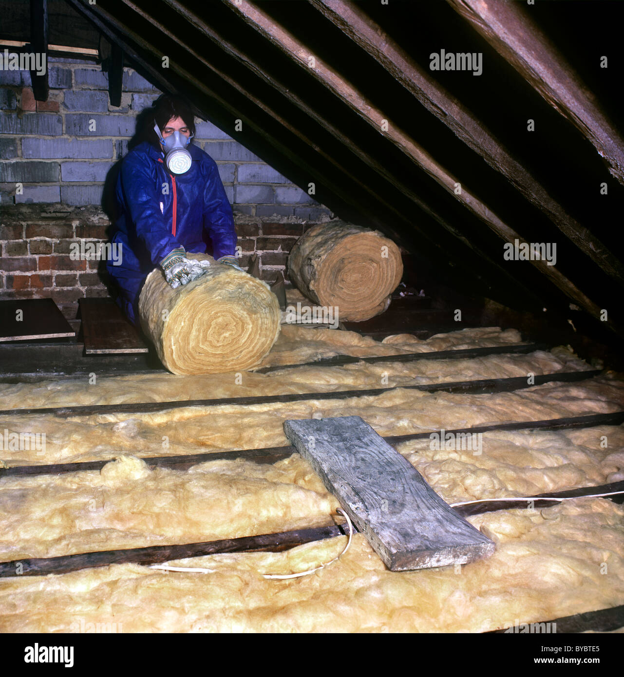 Woman (with protective clothing, gloves and mask) laying insulation material in an old house loft. Stock Photo