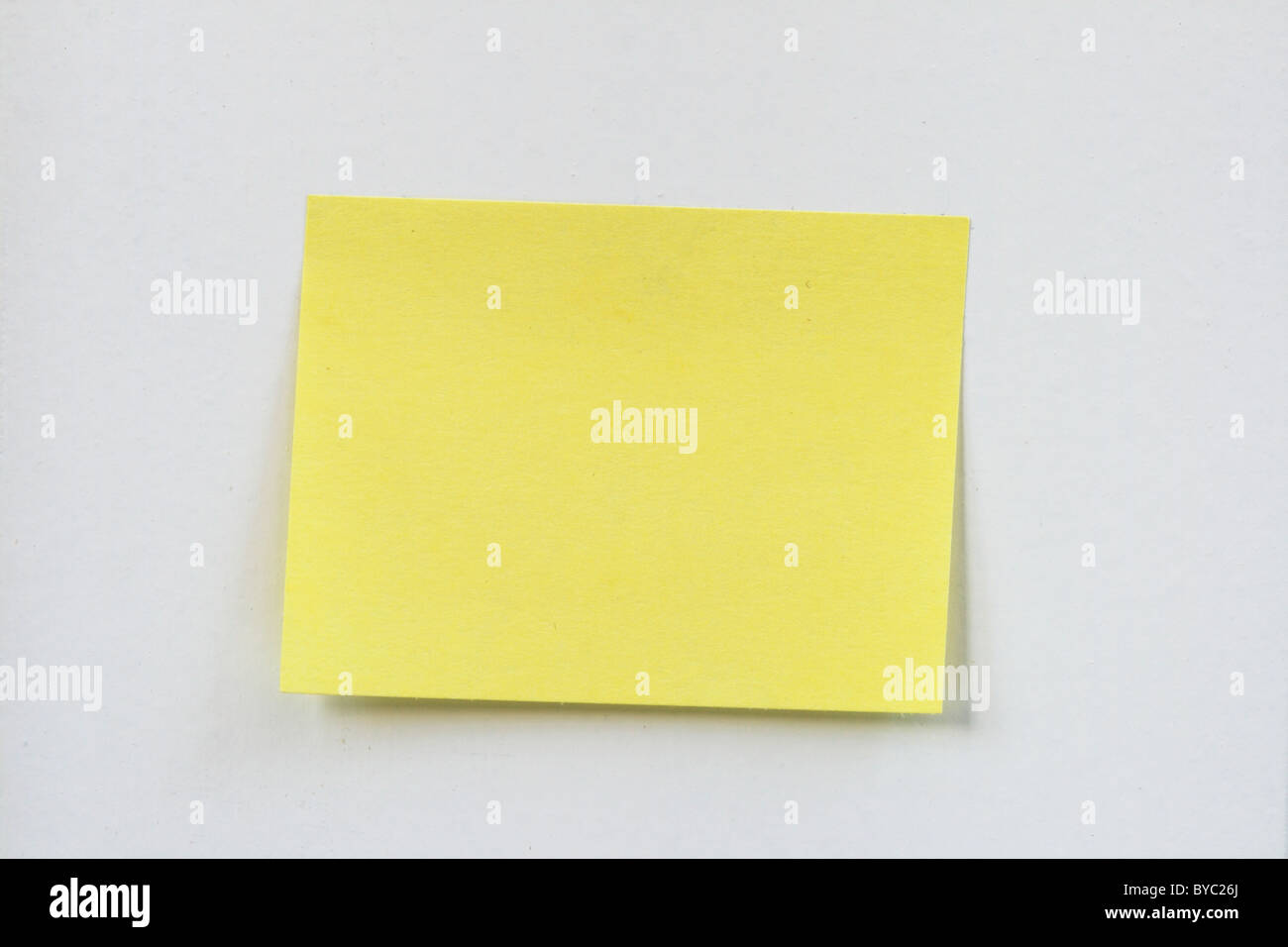 closeup of a small blank yellow sticky note stuck on a white wall Stock Photo