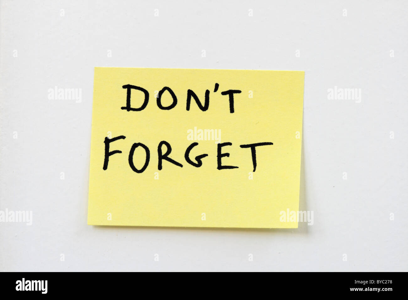 don't forget on a small yellow sticky note stuck on a white wall Stock Photo