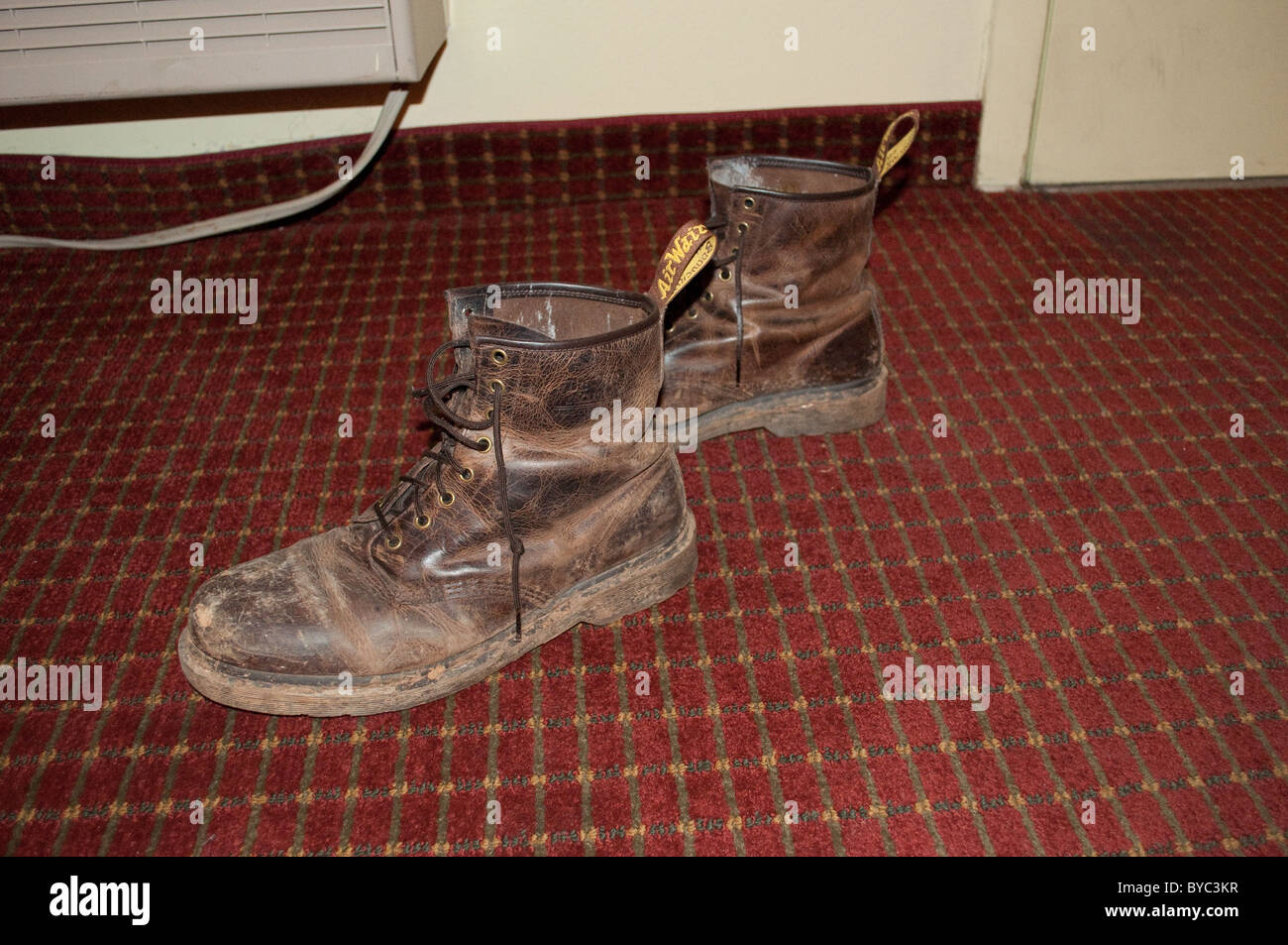 Worn leather work boots on the floor of a nasty roach motel. Stock Photo