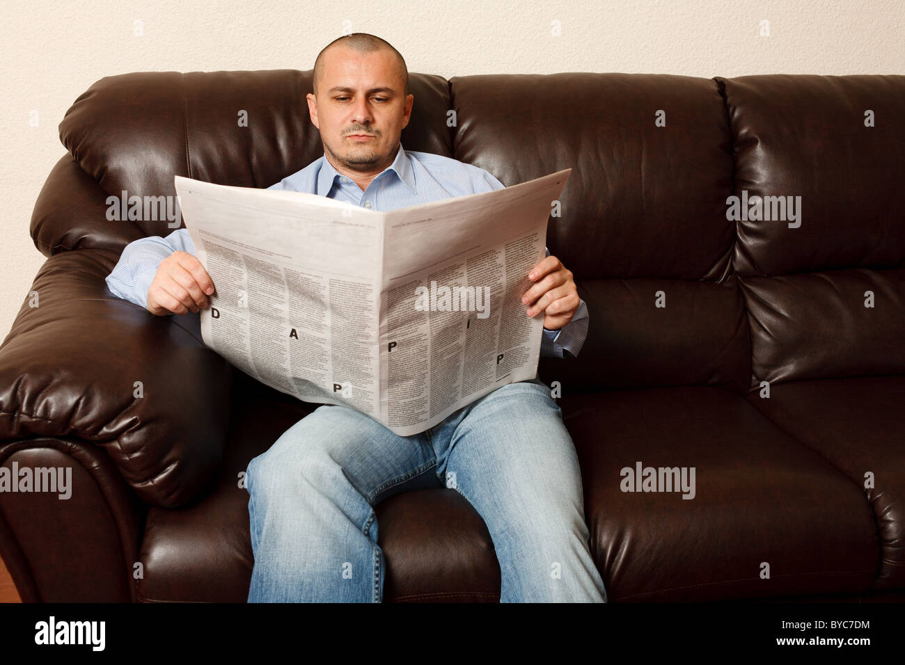 Young man reading newspaper on a leather sofa Stock Photo - Alamy