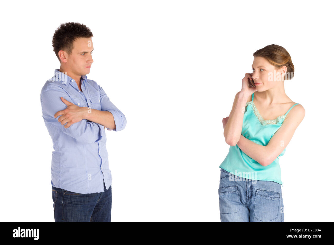 Impatient man standing with arms crossed looking at his girlfriend listening on the mobile phone Stock Photo