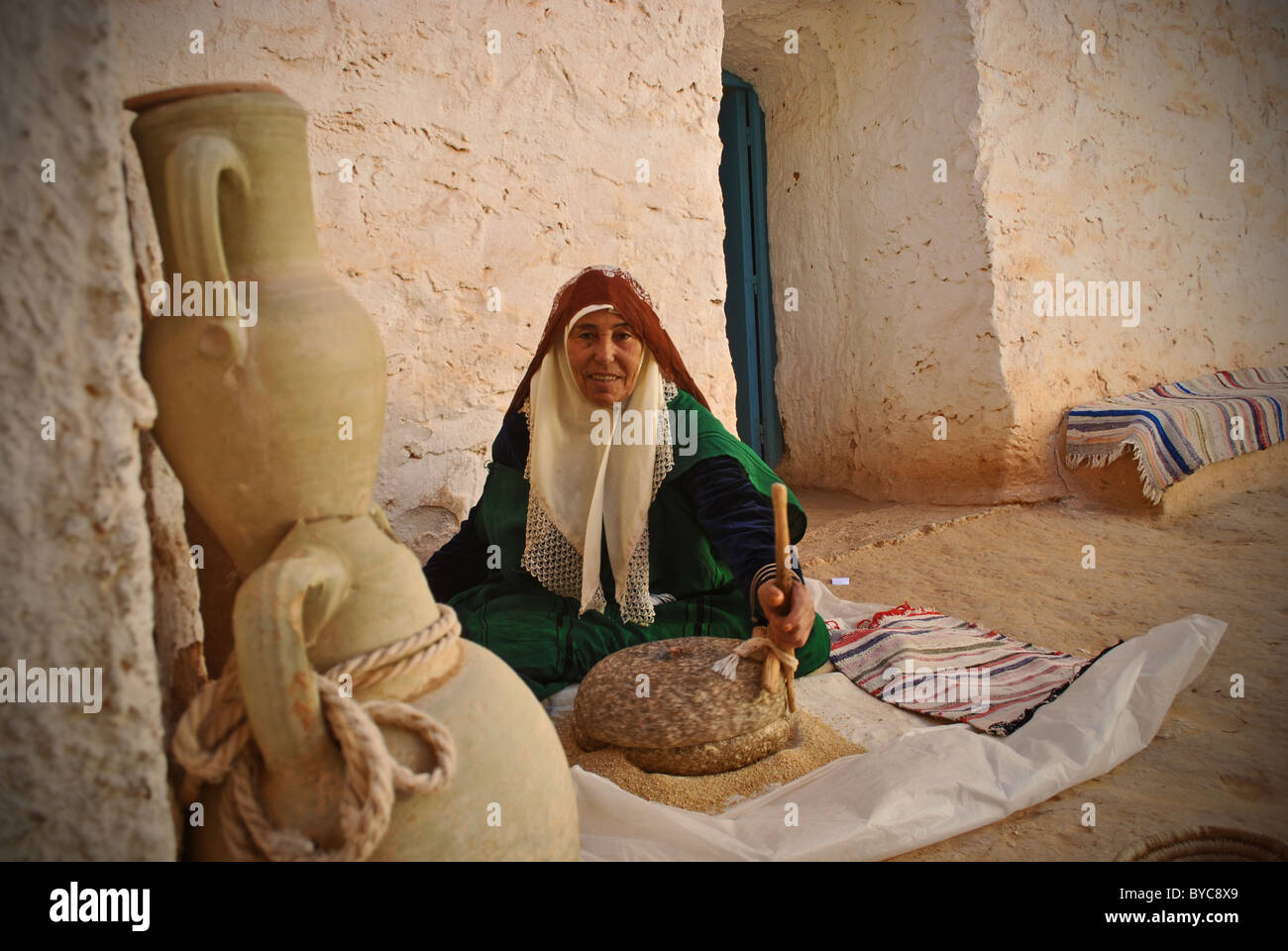Elderly troglodyte woman grinding corn in her home near Matmata Stock Photo