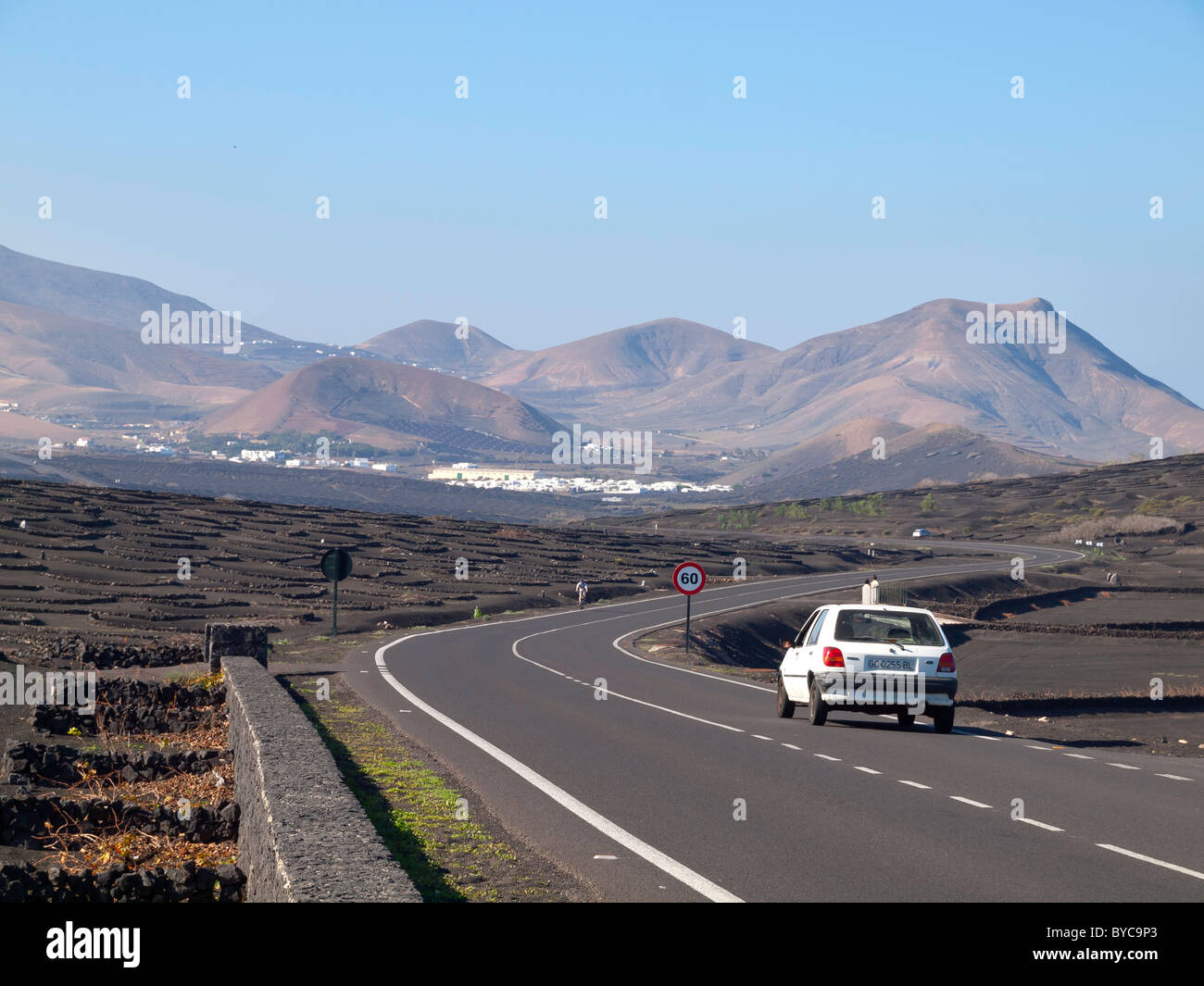 A car on the winding road through La Geria the wine growing region of Lanzarote with the village of Uga in the distance Stock Photo