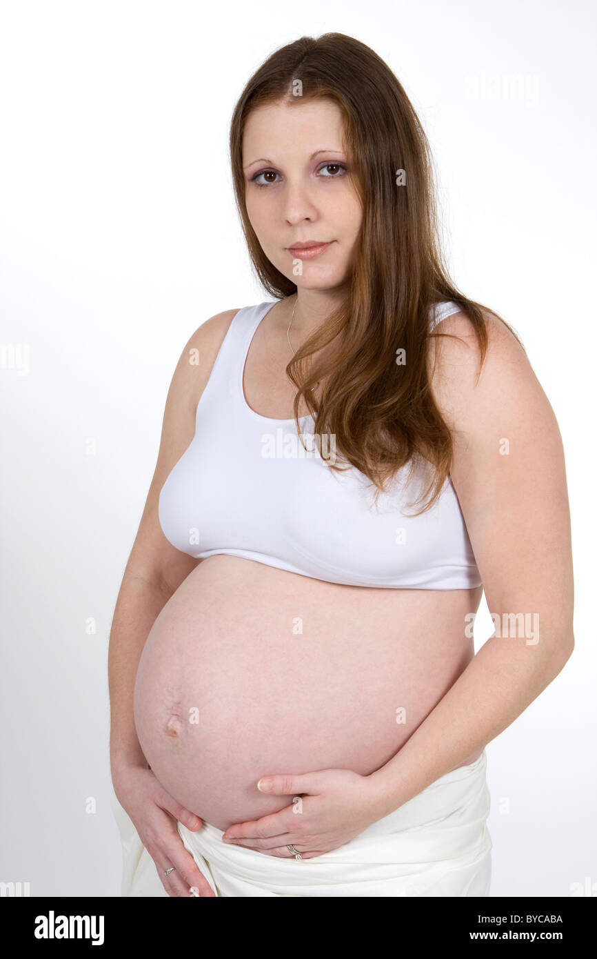 A young pregnant woman holds her swollen belly wearing a sports bra. Stock Photo