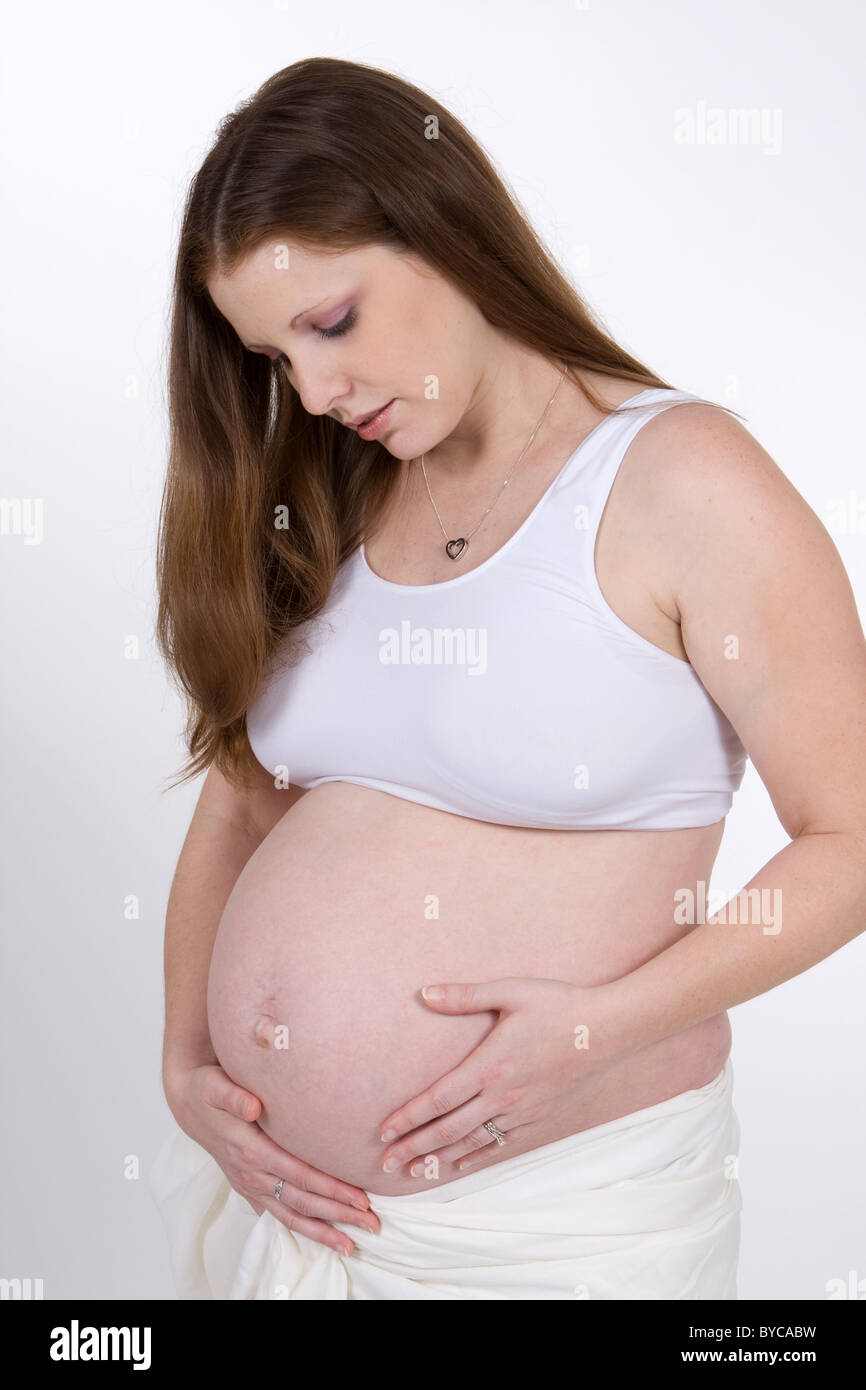 A young attractive pregnant woman holds her abdomen and thinks about her quickly approaching childbirth. Stock Photo