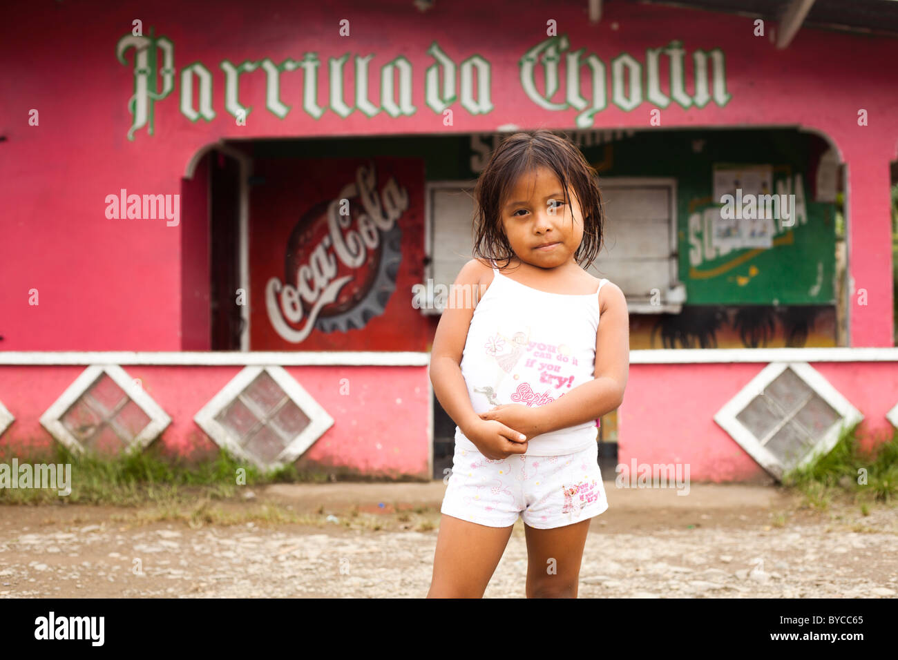 Young girl in white clothes standing in front of pink shot in Panama with coca cola sign Stock Photo