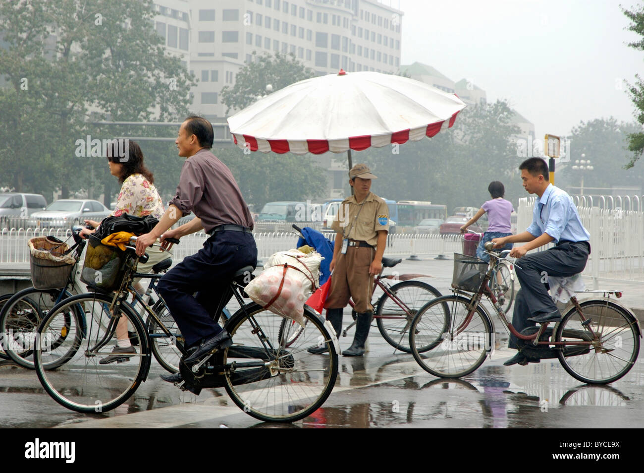 Beijing Traffic warden watching cyclists cycling by in the rain, Beijing, China. Stock Photo