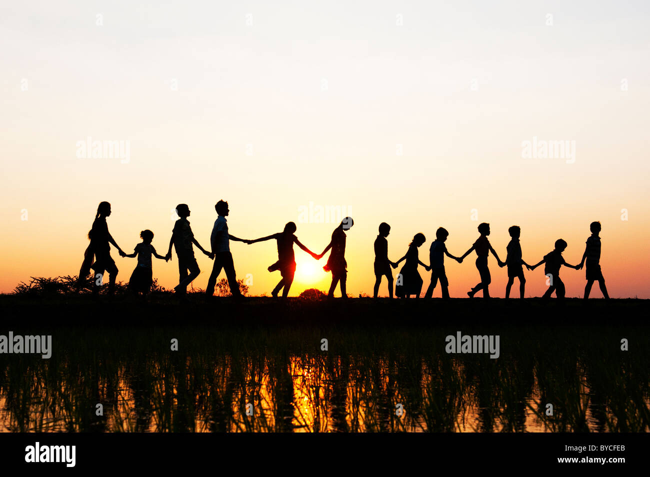 Silhouette Indian girls and boys holding hands walking home across a rice paddy field at sunset. Andhra Pradesh, India Stock Photo