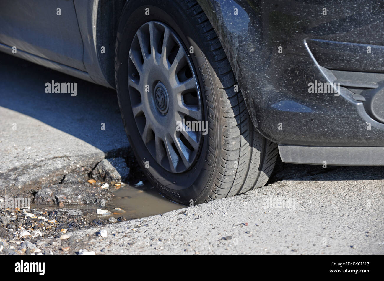 A car tyre sits in a deep pothole in a busy road caused by the recent