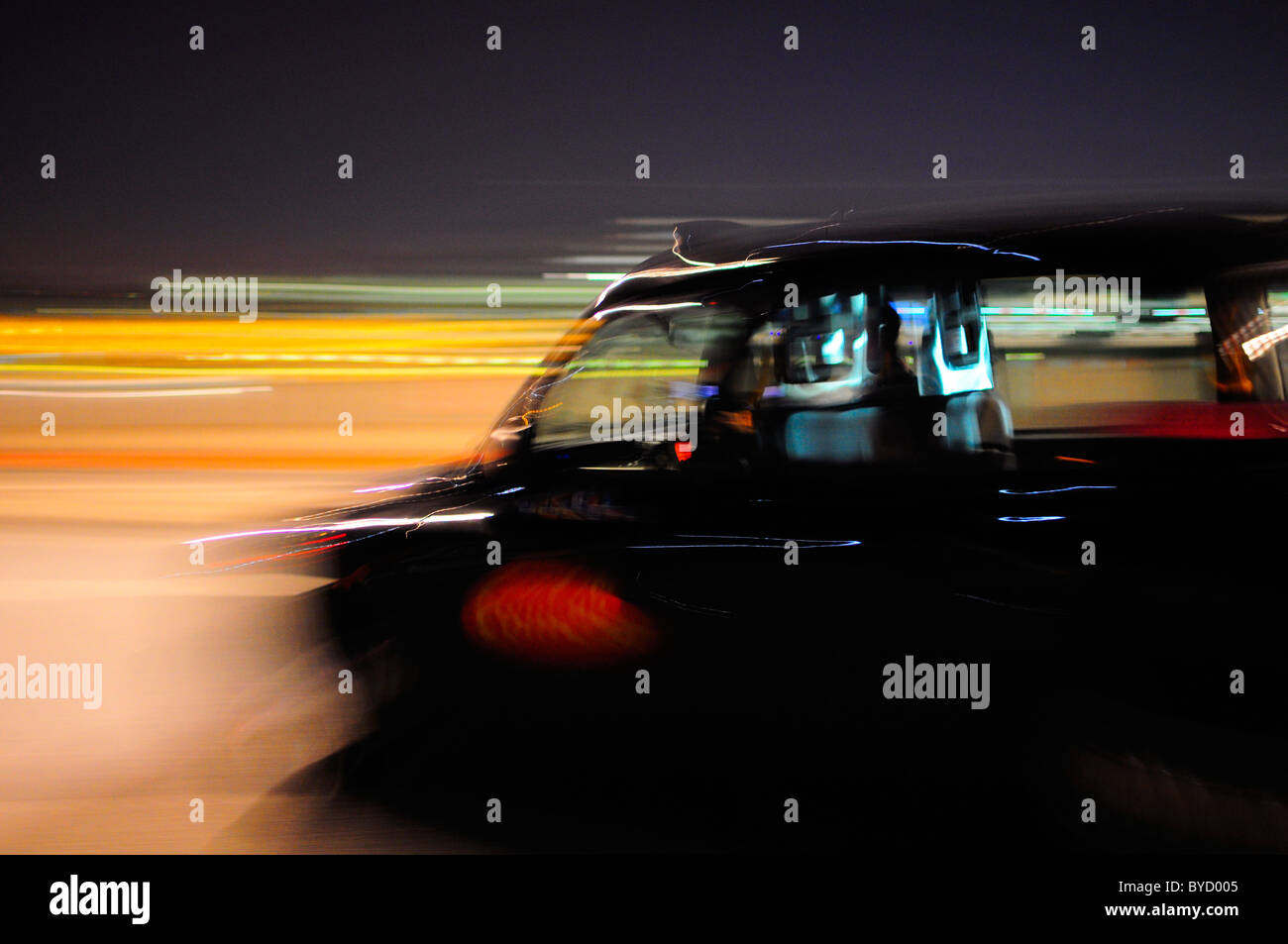 Black Taxi Cab moving through the streets of London at Night with motion blur Stock Photo