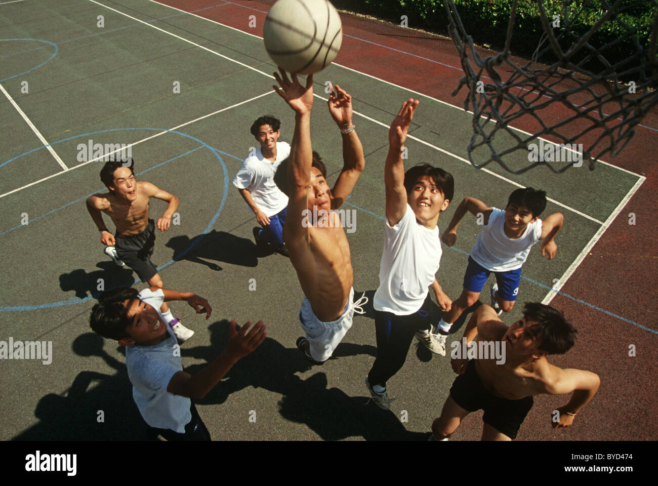 Teenage students jump high on basketball court to score a goal at the Gyosei International Japanese School, Milton Keynes. Stock Photo
