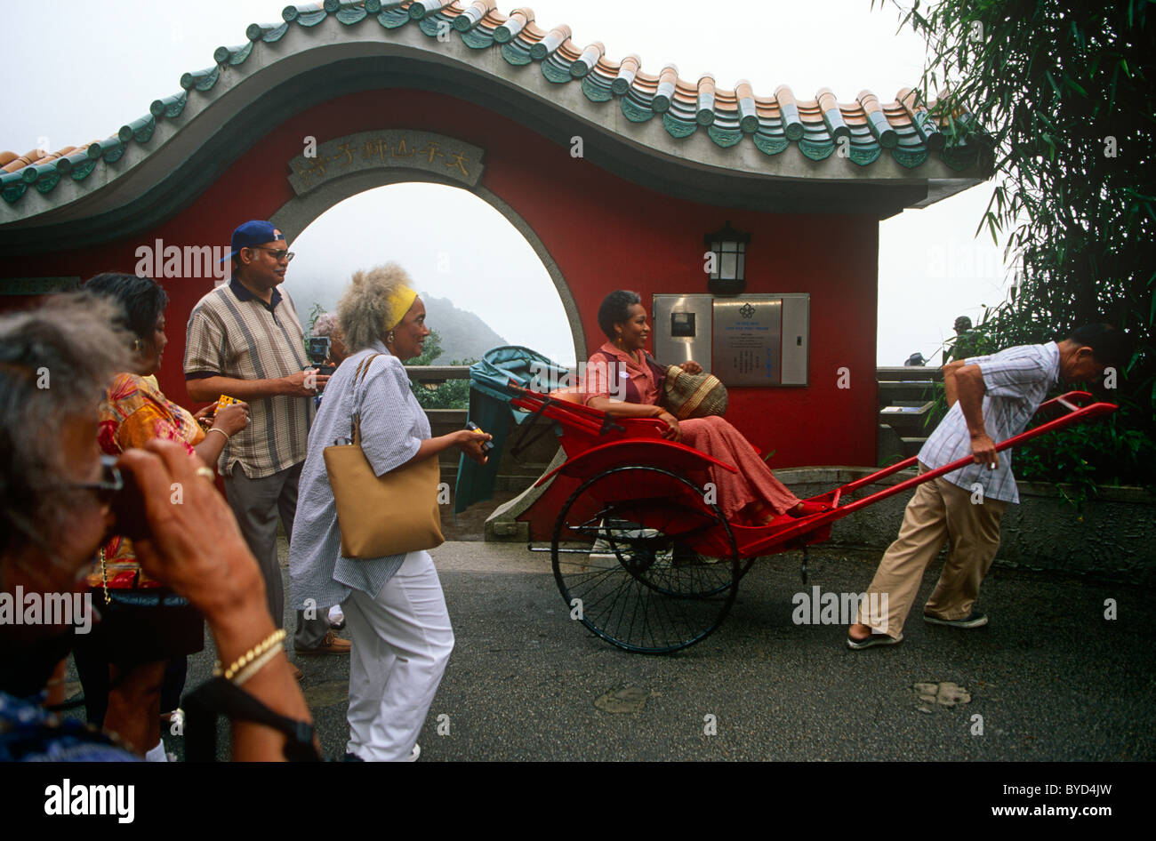 American tourists admire one of their number riding who has hired a rickshaw on Hong Kong's Peak. Stock Photo