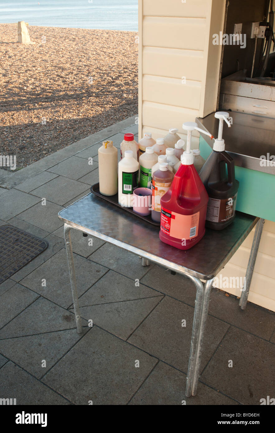 Seaside fish and chip kiosk, a table laden with sauce bottles, the beach and sea in the background. Stock Photo