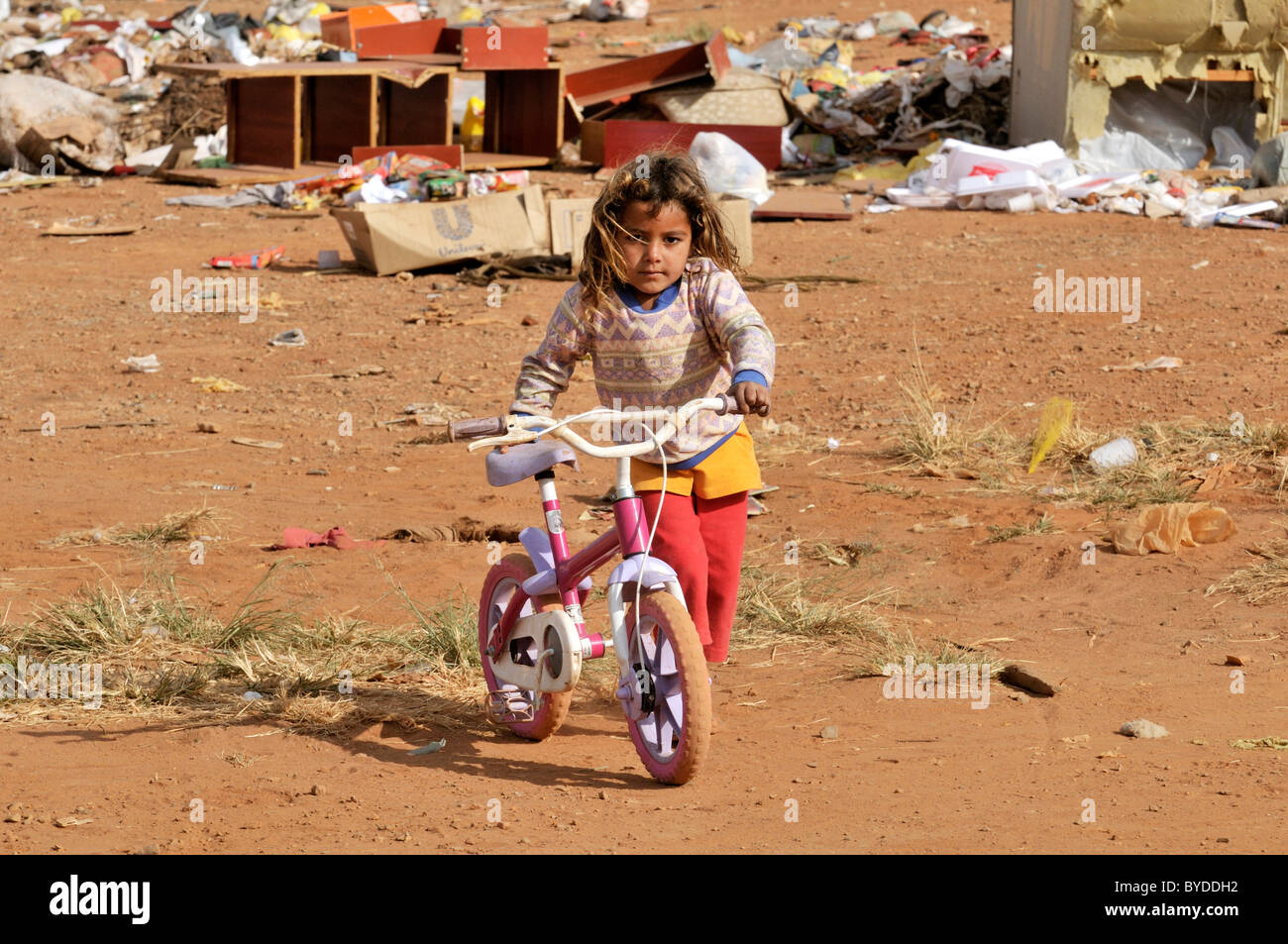 Girl, 8, pushing a pink bike, which she found at the informal garbage dump outside her home, her family lives by collecting, Stock Photo