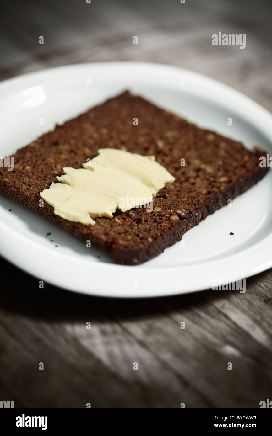 Dark wholemeal bread on a white plate with a little butter Stock Photo