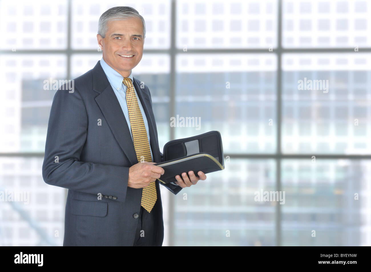 Standing Middle Aged Businessman with Planner Notebook in Modern Office Setting. Stock Photo